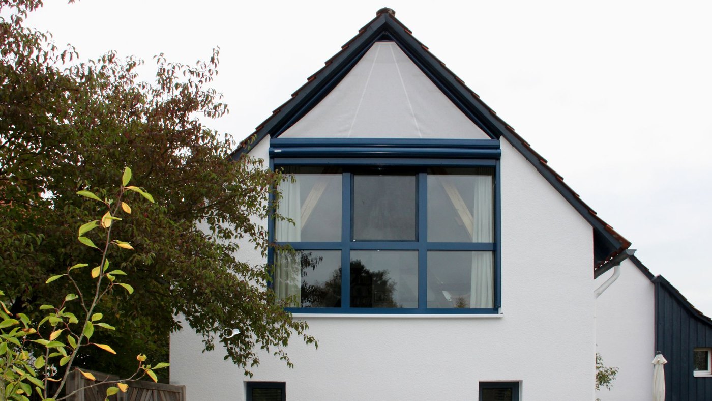 Hvidt hus med trekantet gavlvindue og forlænget Markilux 893 vinduesmarkise